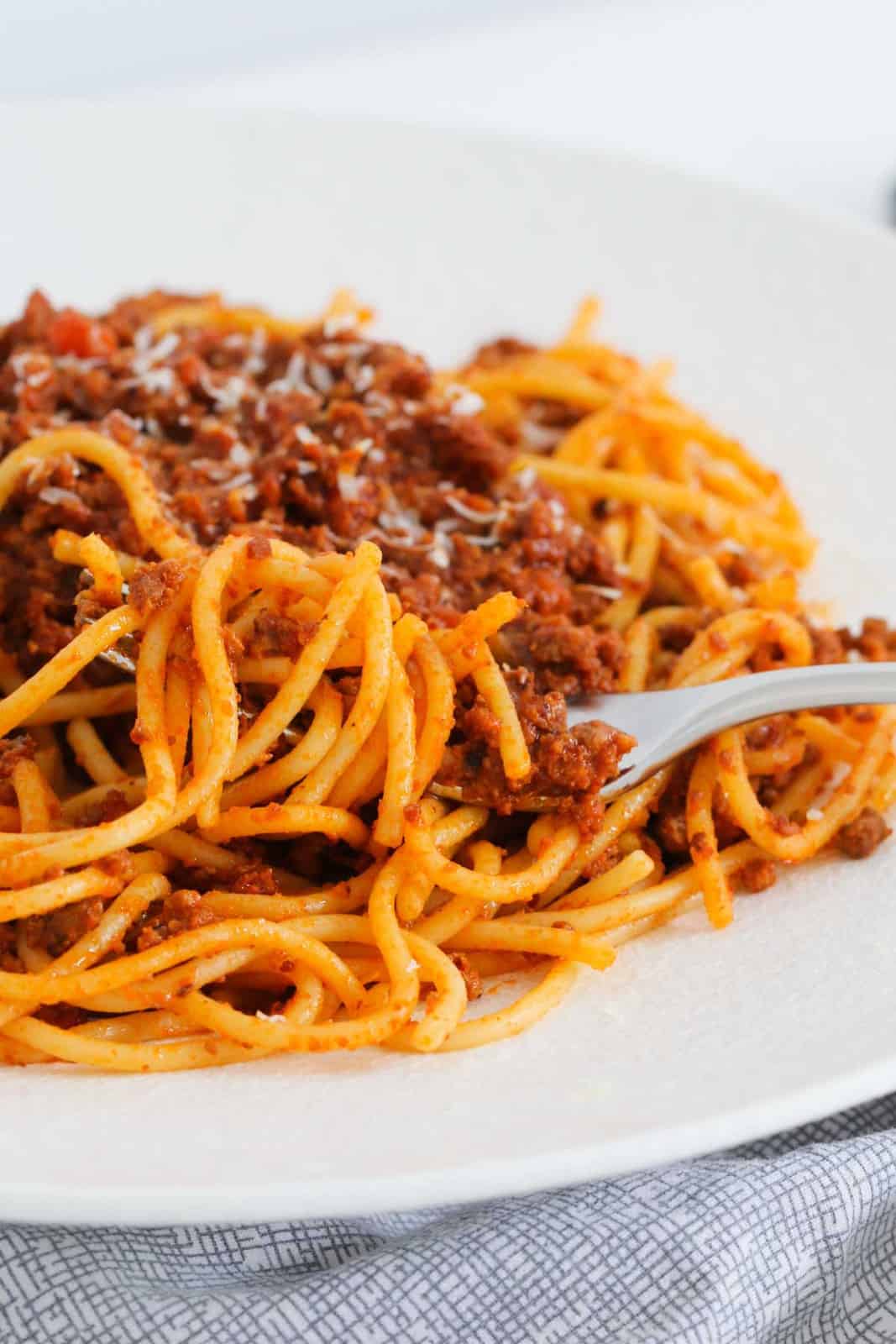 A forkful of bolognese with pasta on a white plate.