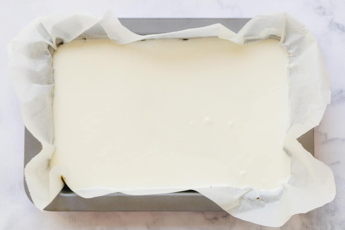 White chocolate spread over a slice in a lined baking tray