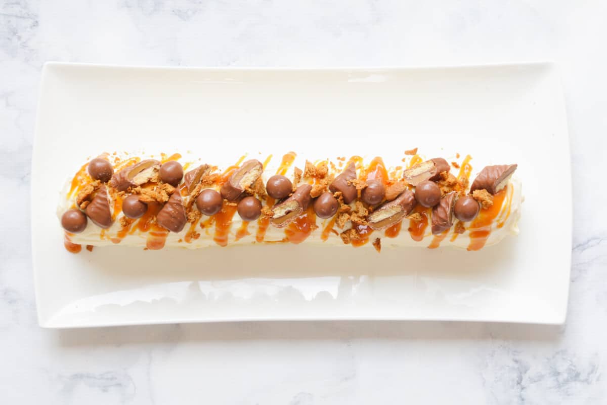 An overhead shot of a cream log decroated with chocolates and caramel sauce.