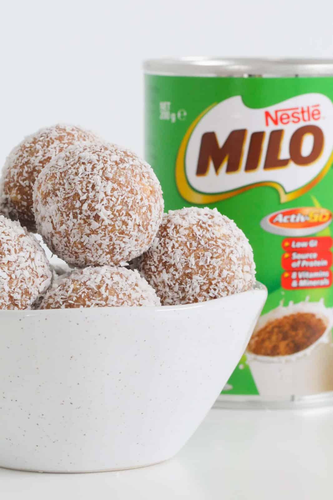 A bowl filled with malted milk and coconut balls, with a tin of Milo malted milk powder in the background.