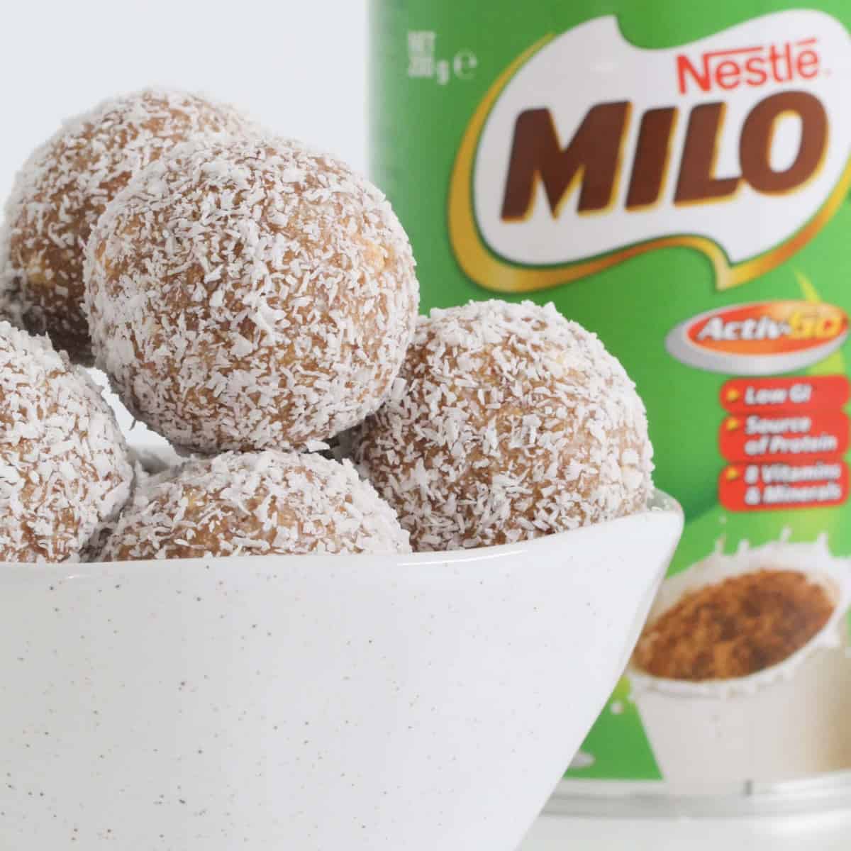 A bowl filled with coconut covered balls with a Milo tin in the background.