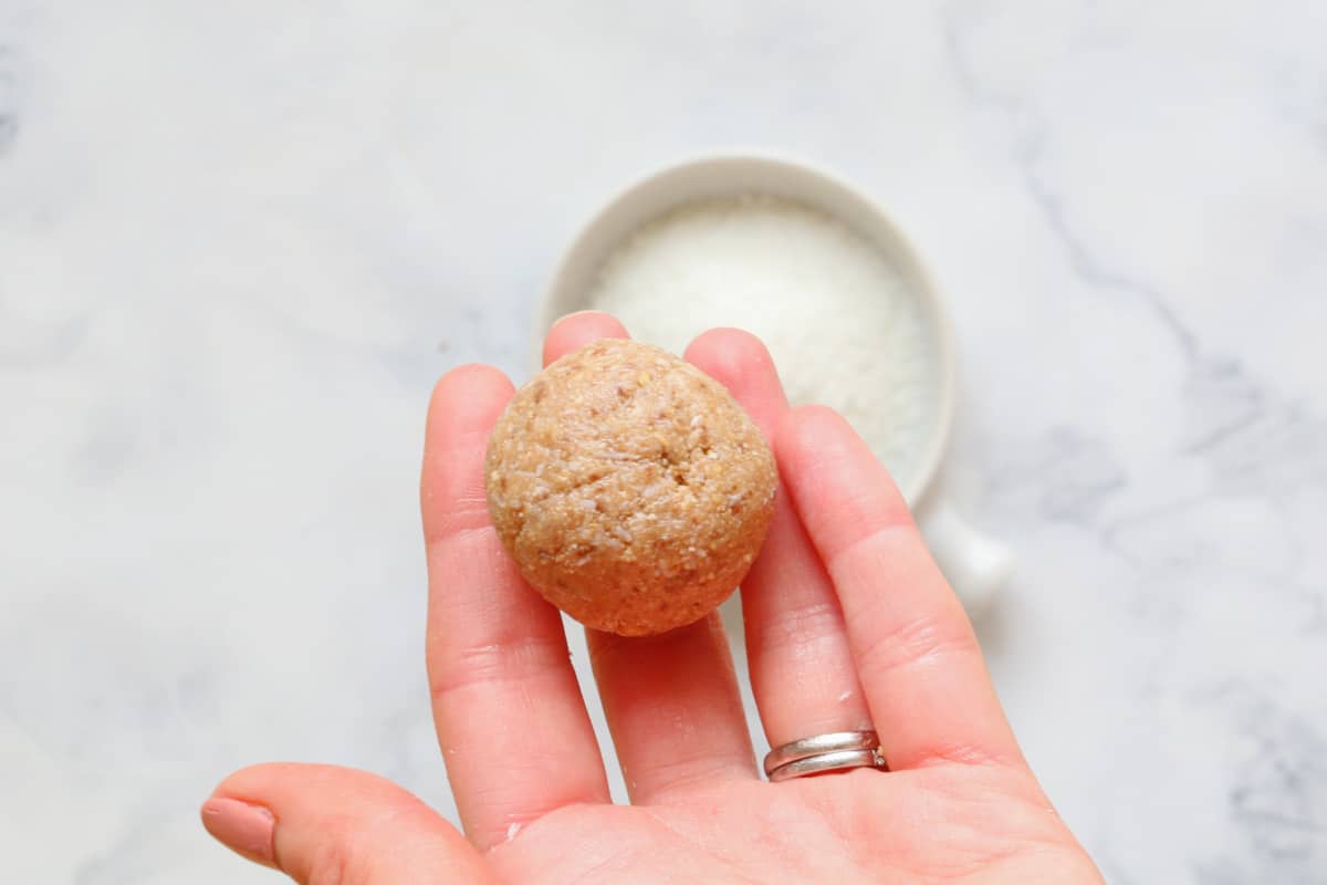 A sweet ball made of crushed biscuits, Milo, condensed milk and coconut, held in an outstretched hand.