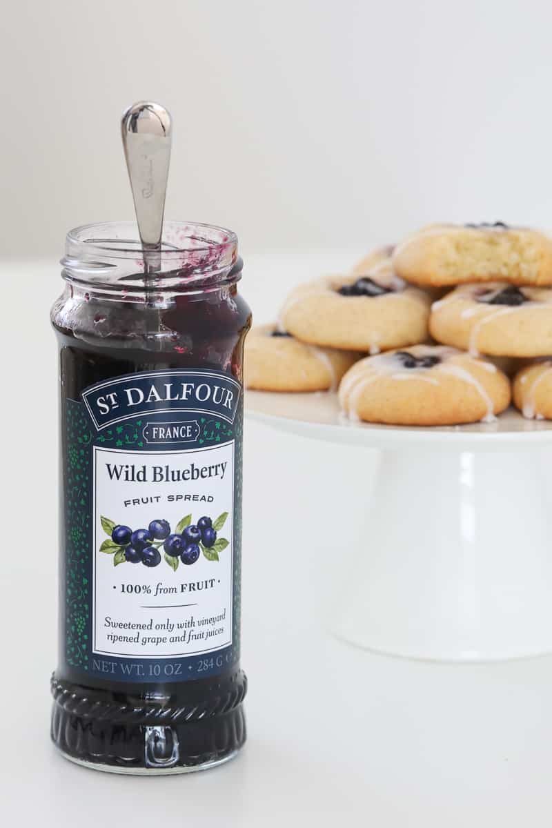 A jar of blueberry fruit spread in front of a plate of baked cookies.