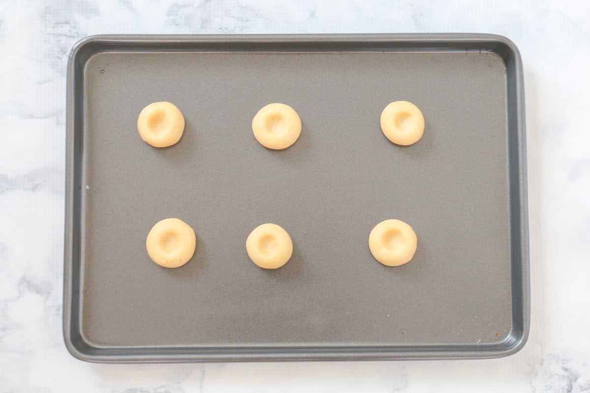 Cookie dough balls with indents in the centre on a baking tray.