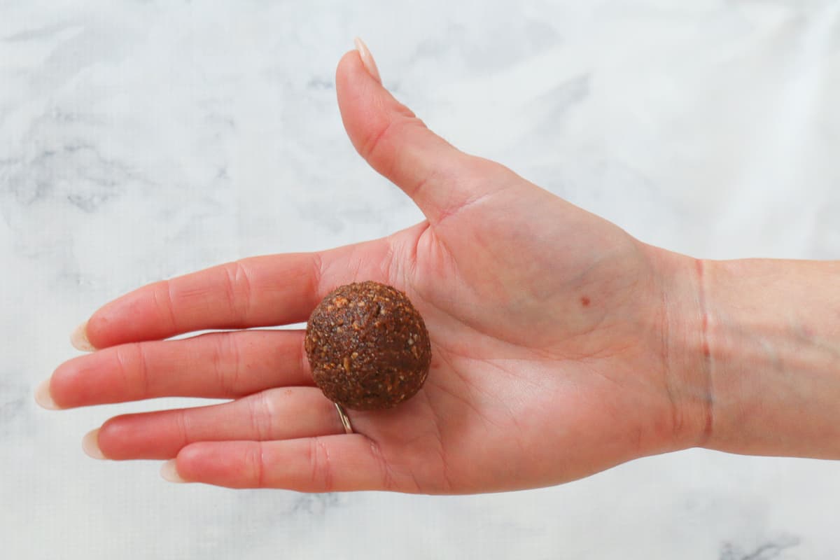 A hand holding a rolled chocolate date and almond bliss ball.