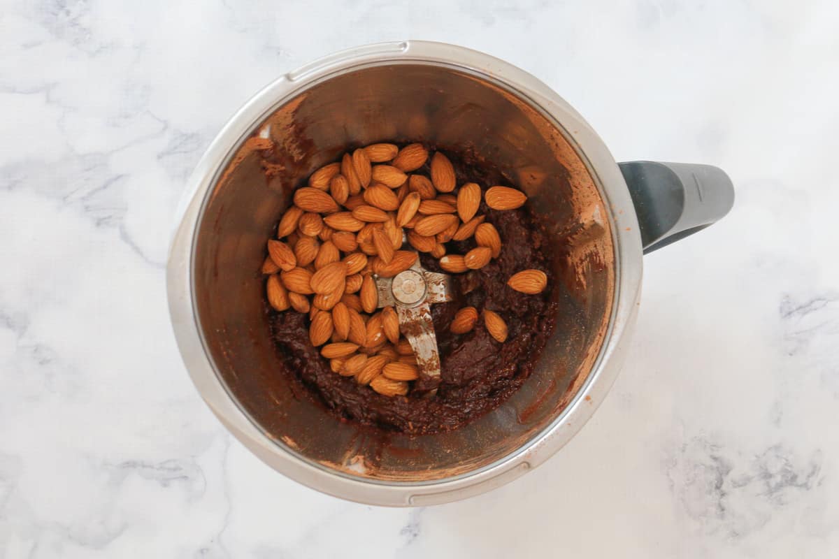 Almonds on top of a chocolate and date paste in a Thermomix bowl.