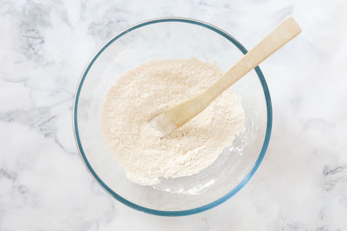 A wooden spoon in a glass bowl of flour mixture.