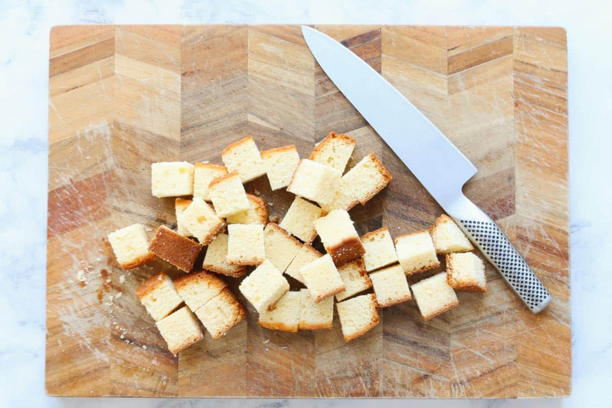 A knife on a chopping board next to chunks of Madeira cake.