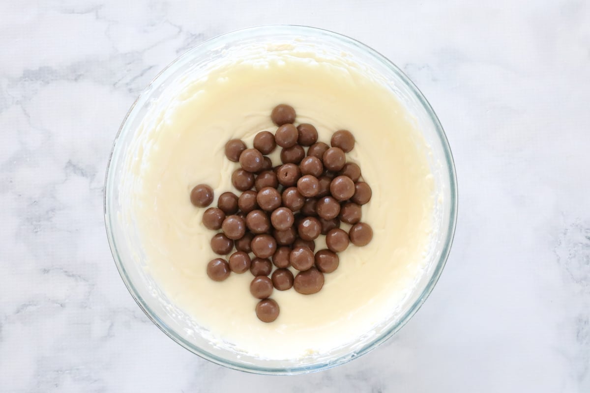 Malteser on cheesecake mixture in a bowl.
