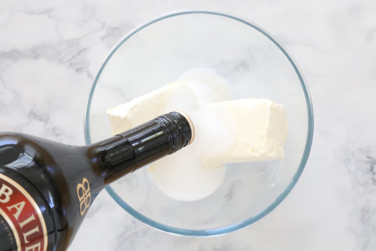 Baileys being poured on top of cream cheese and sugar.