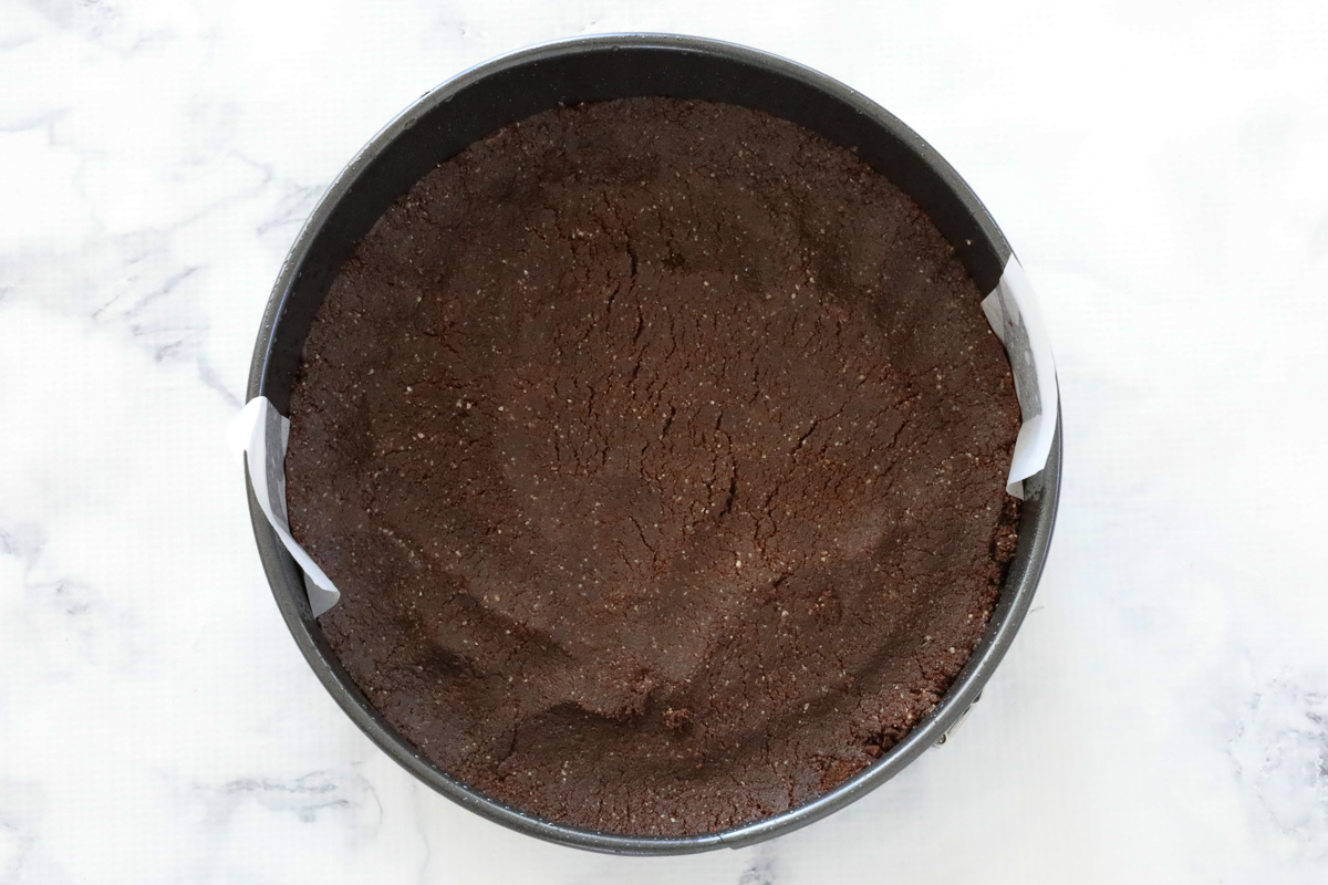 Chocolate biscuit crumbs pressed into a springform pan.