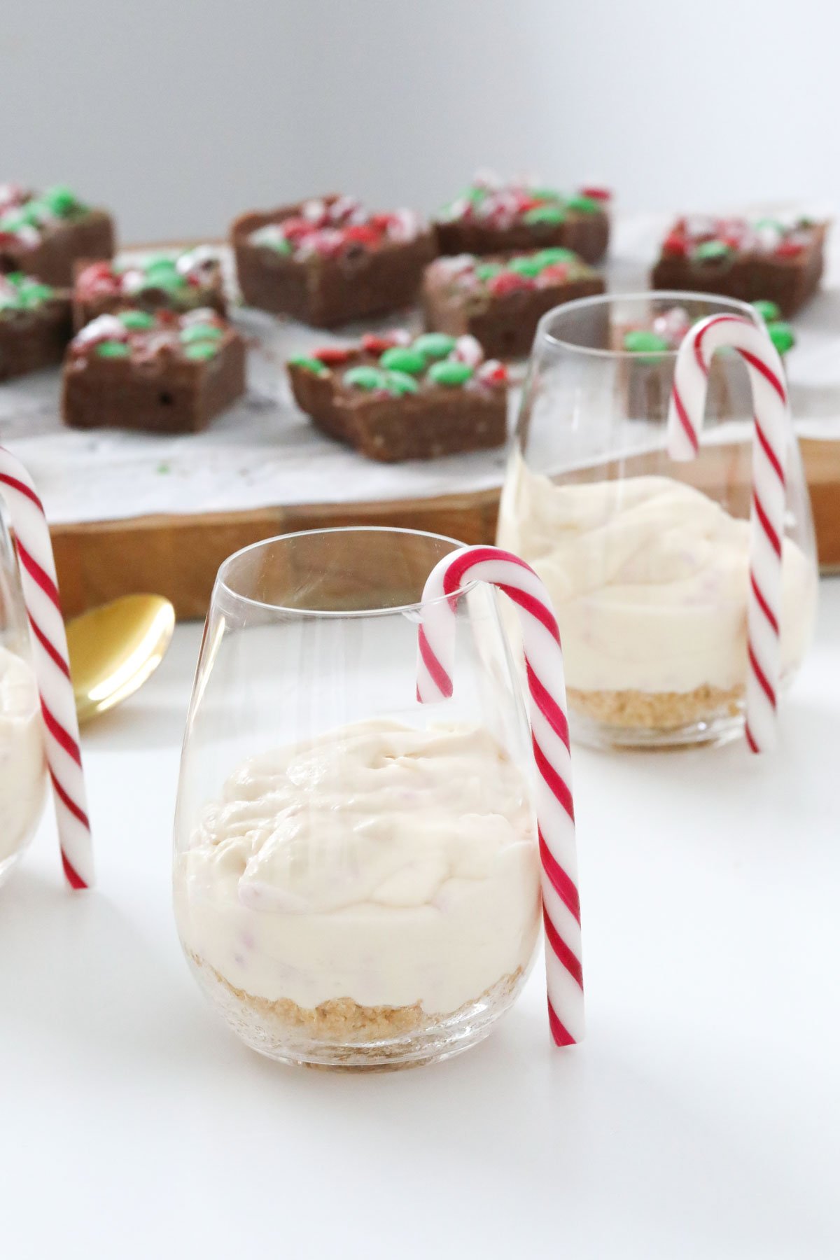 Dessert glasses with a striped candy cane hanging on the side with individual cheesecakes inside