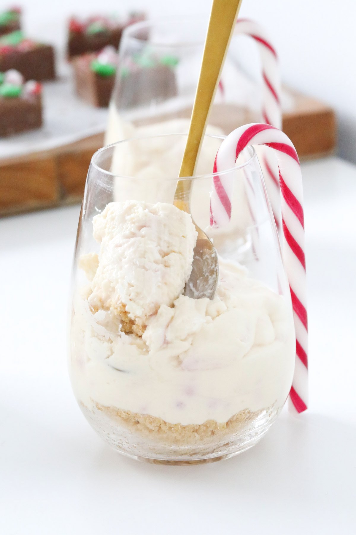 A close up of a stemless wine glass filled with a white cheesecake mixture, and a candy cane placed over the rm of the glass.