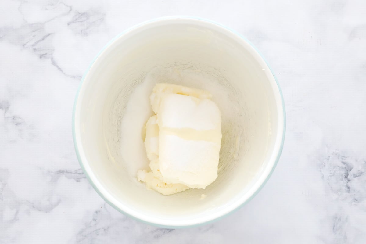 Softened cream cheese and sugar in a white bowl on a marble counter