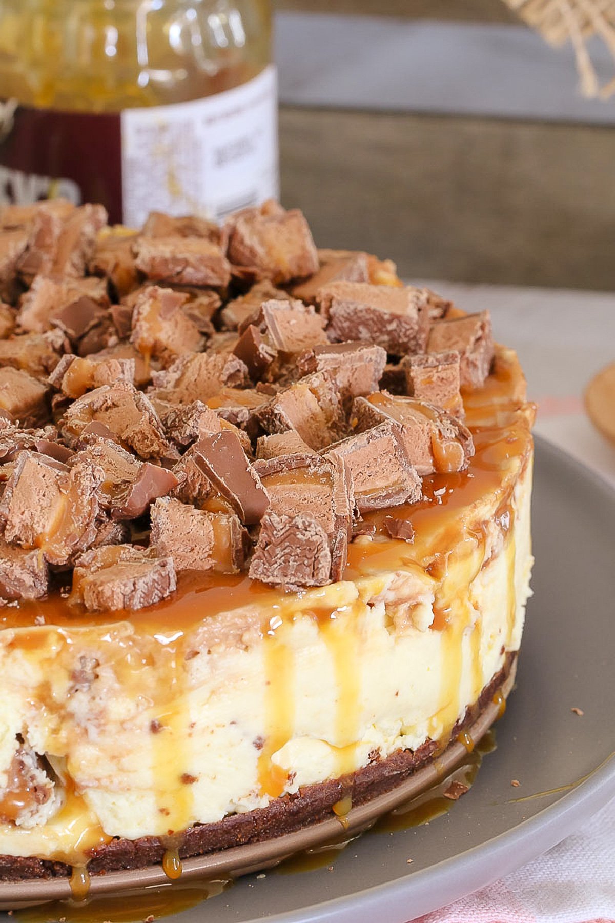 A close up view of a cheesecake topped with chunks of Mars Bars and caramel sauce.