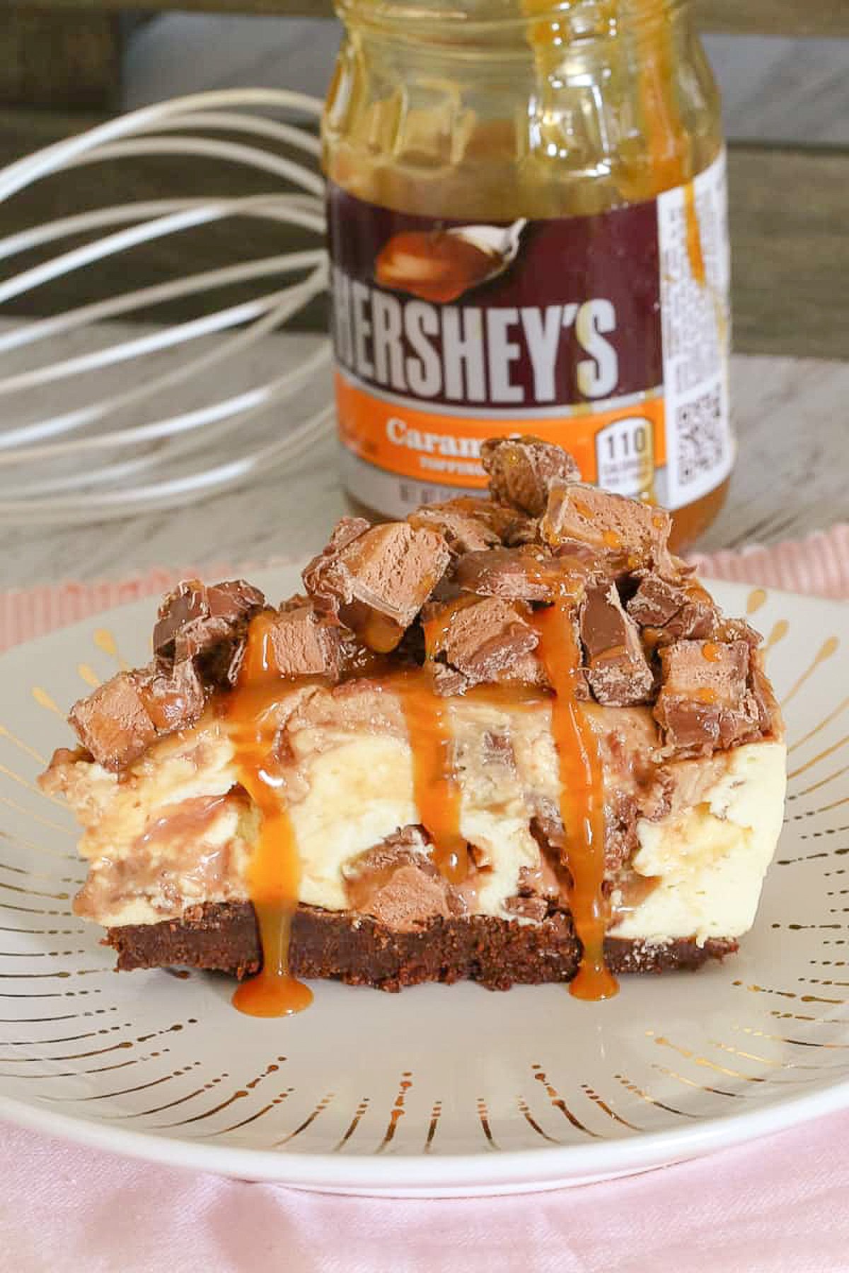 A piece of Mars Bar cheesecake in front of a jar of Herseys's caramel sauce.
