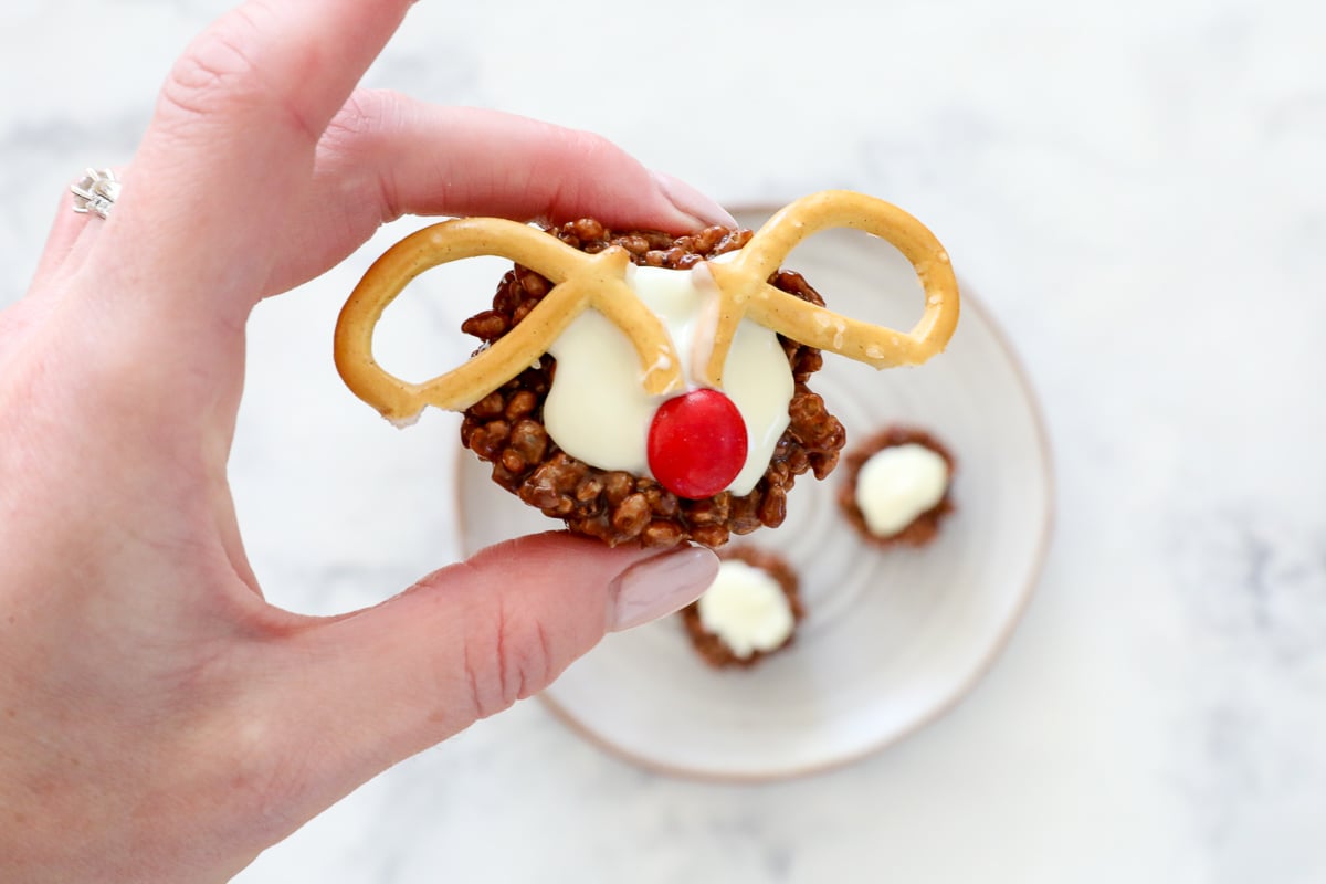 A hand holding a chocolate rice krispie bite decorated like a reindeer.