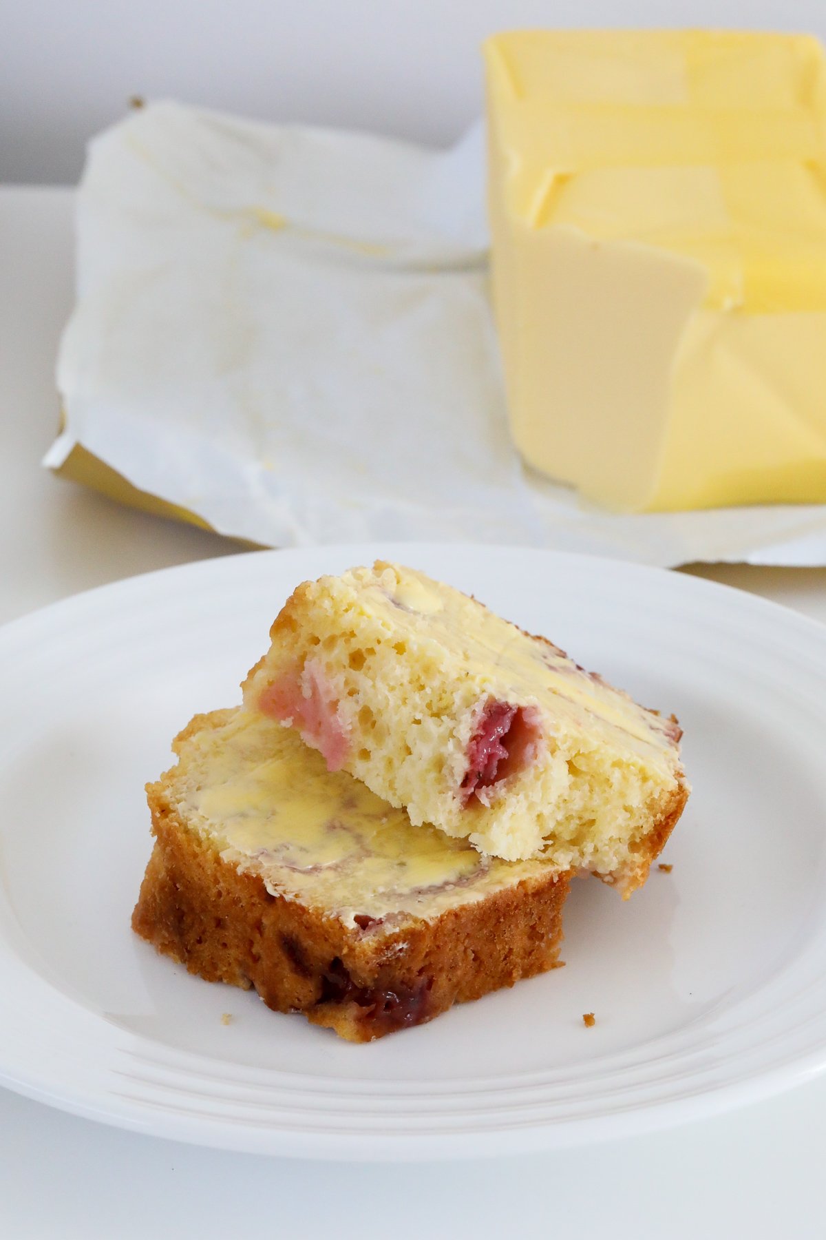 Two slices of strawberry loaf on a plate with butter in the background.