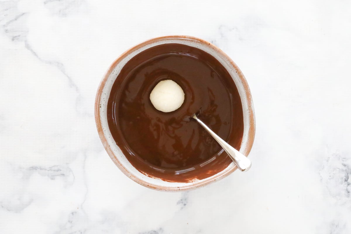A white ball and a spoon in a bowl of melted dark chocolate.