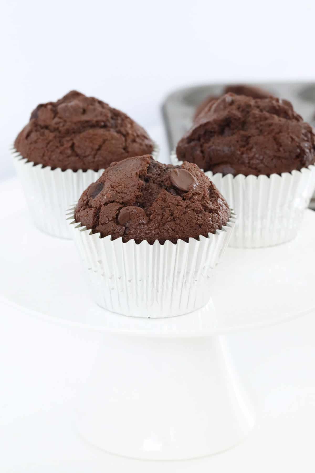 Chocolate muffins in silver muffin cases on a white cake stand