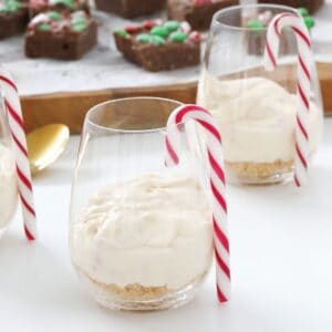 Dessert glasses with a striped candy cane hanging on the side with individual cheesecakes inside