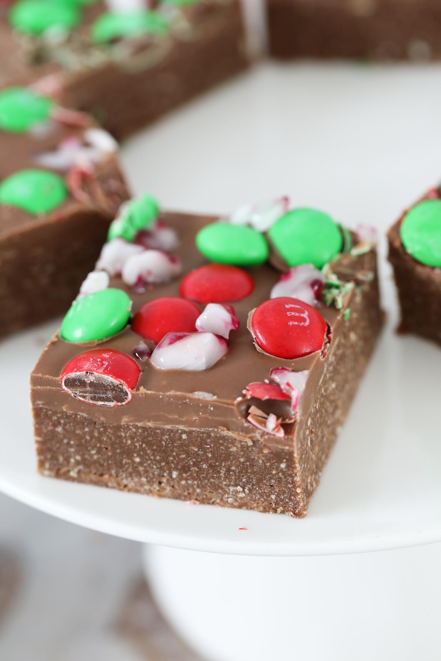A close up of a piece of chocolate slice with milk chocolate, M&Ms and crushed candy canes on top.