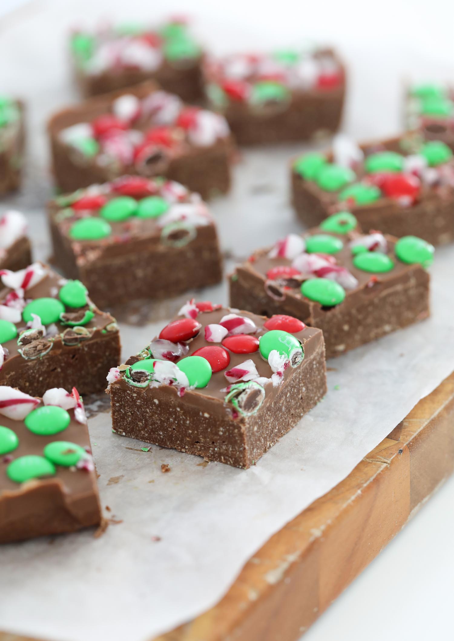 Squares of a chocolate slice on a wooden board topped with red and green M&M's.