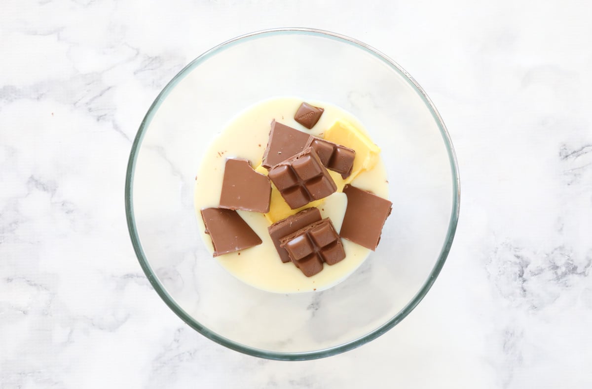 Condensed milk, butter and chunks of peppermint chocolate in a glass bowl