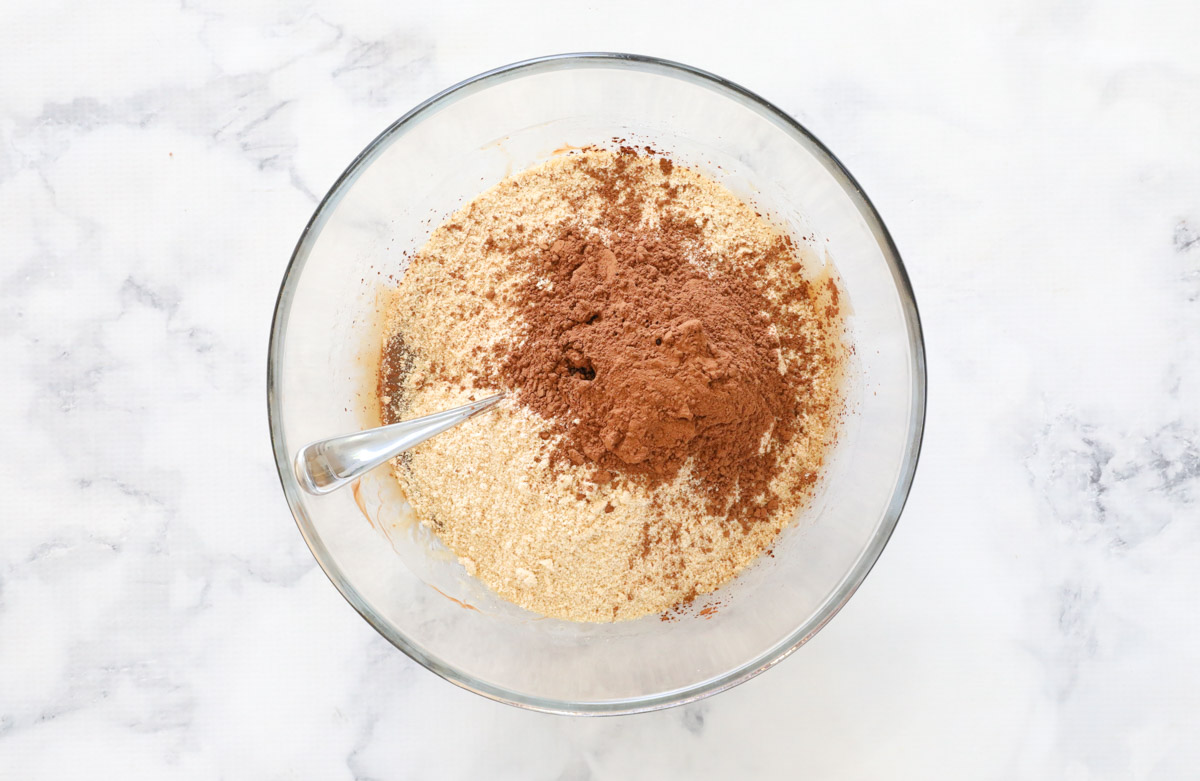 Crushed biscuits and cocoa powder added to melted chocolate mixture in a glass mixing bowl