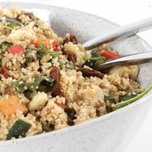 Salad servers in a bowl of couscous salad with roast vegetables.