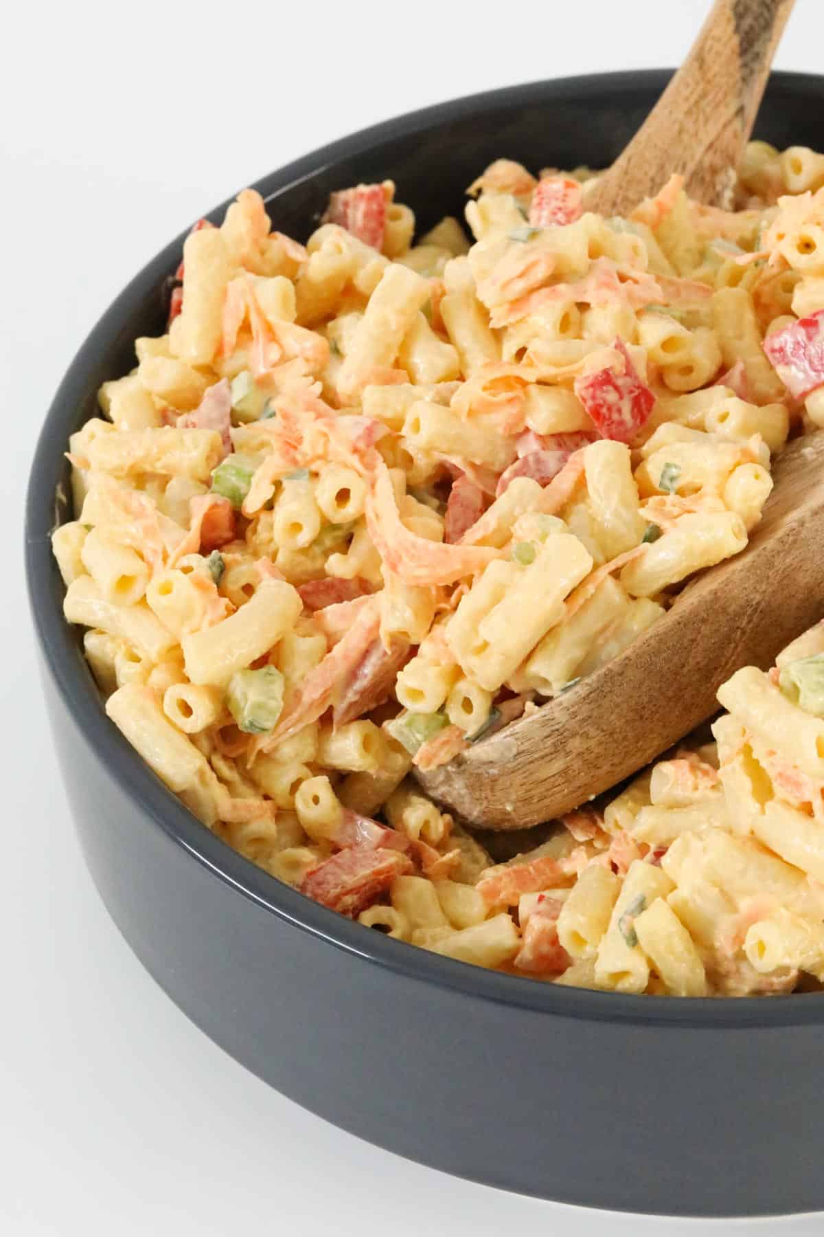 Pasta salad in a black bowl with wooden serving spoons
