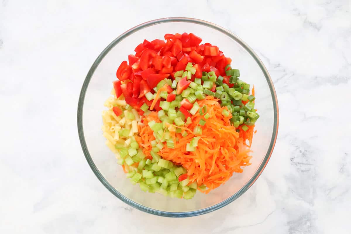 Chopped vegetables added to cooked macaroni in a glass bowl