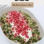A grain salad topped with a Greek yoghurt dressing and scattered with pomegranate seeds, served in a white oval dish.