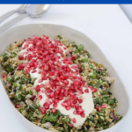A bowl of summer salad made with grains, herbs, seeds and nuts, topped with a yoghrt dressing and pomegranate seeds