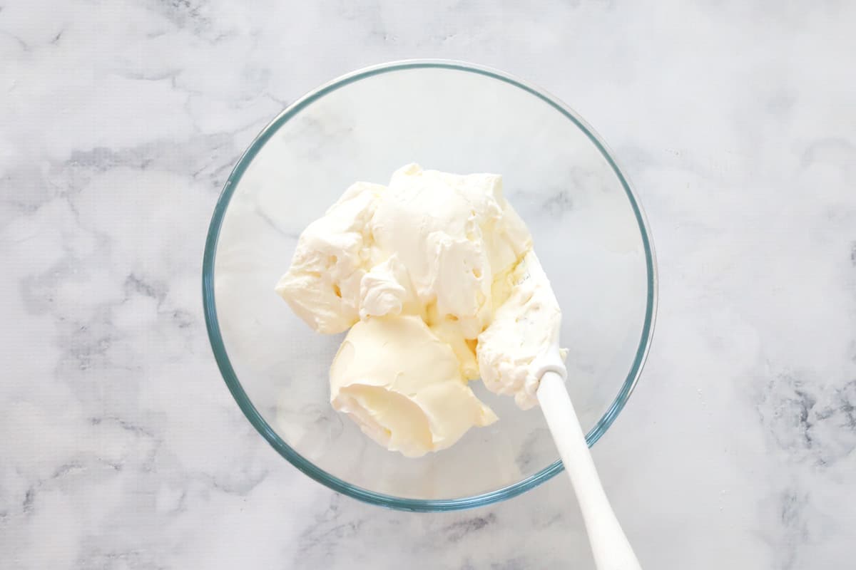 whipped cream and mascarpone in a glass bowl with a spatula