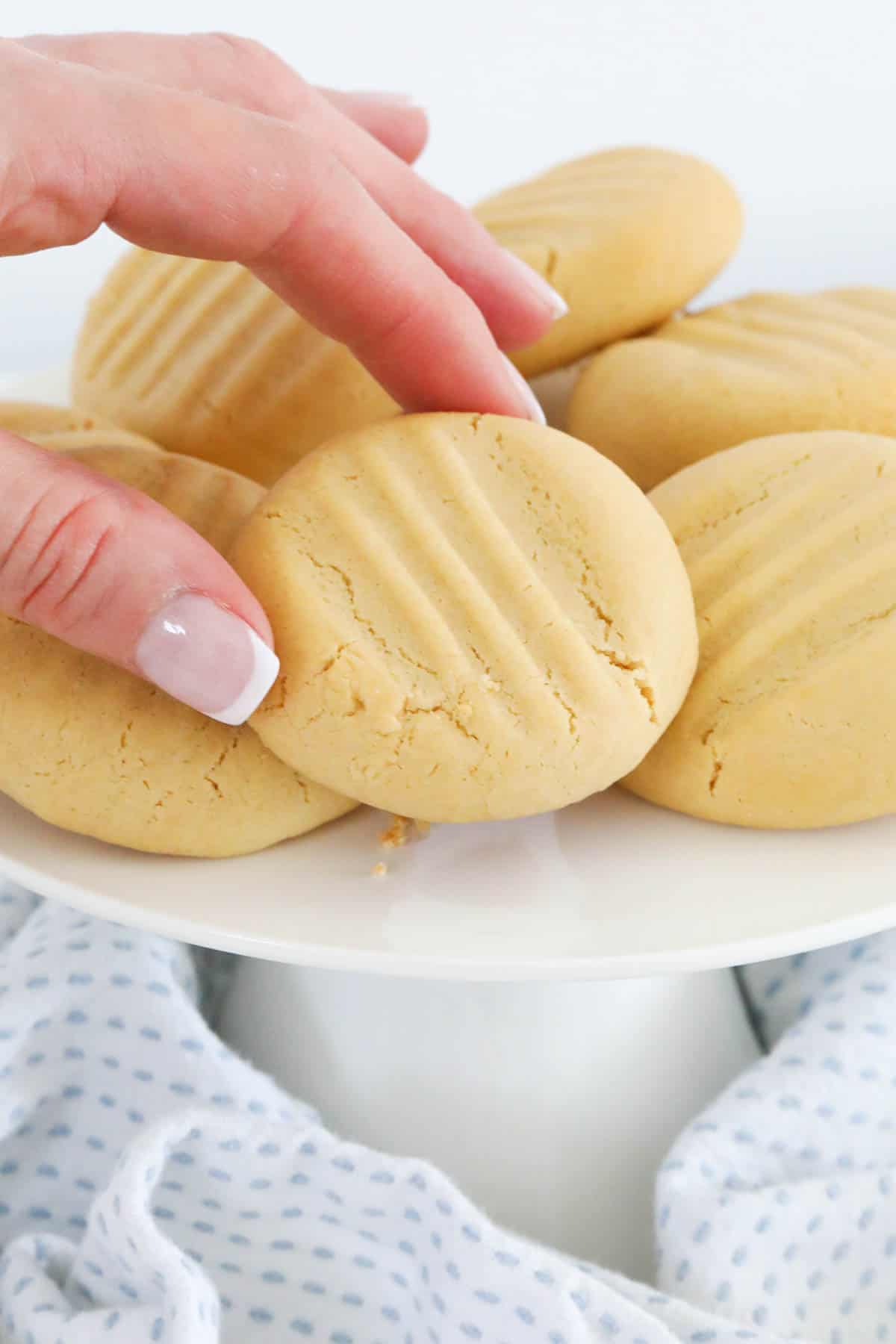 A hand reaching out and picking up a golden biscuit from a plate.