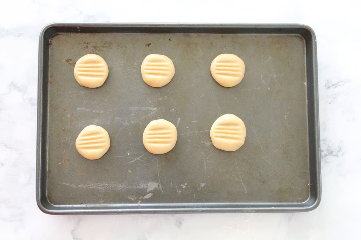 Small round balls of biscuit mixture, flattened with a fork and placed on a baking tray.