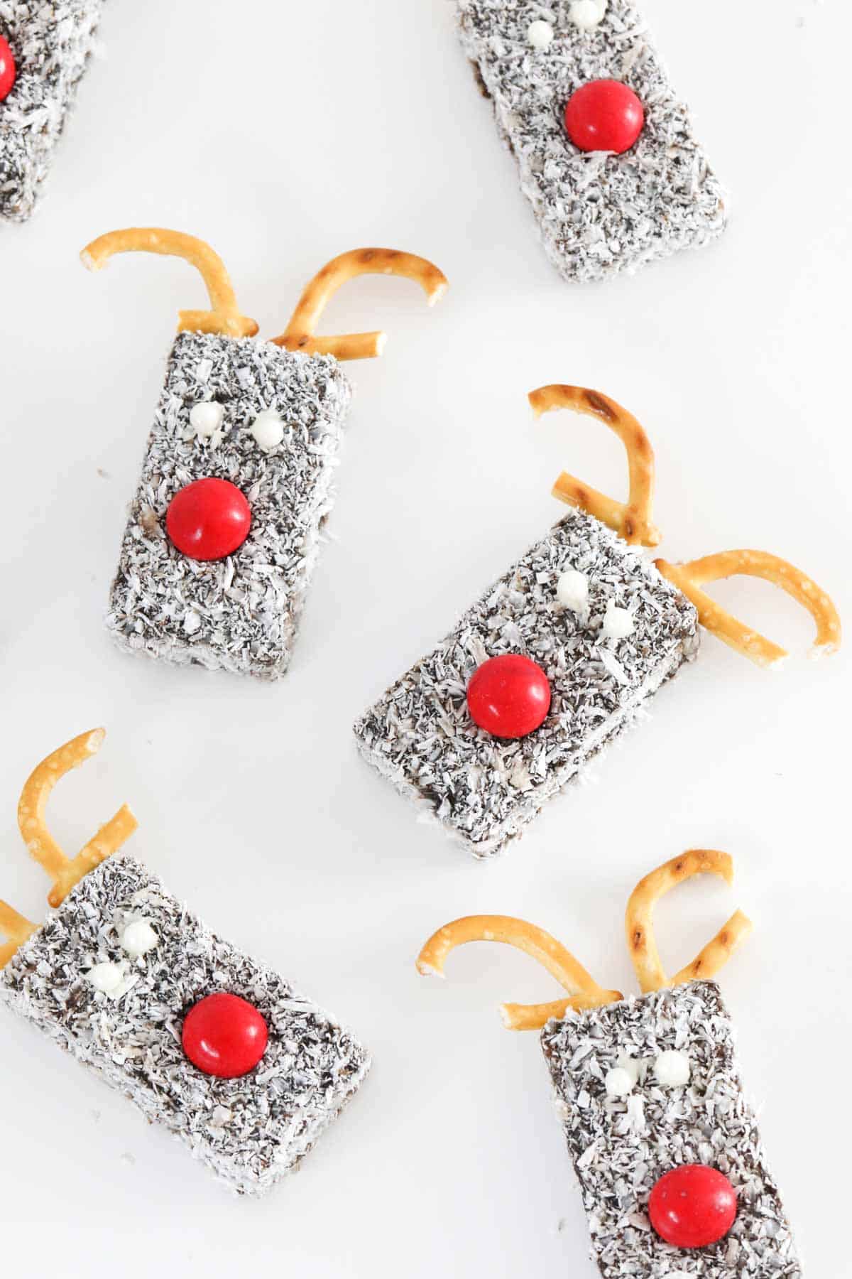 A white background with edible reindeers made out of chocolate and coconut coated sponge fingers.