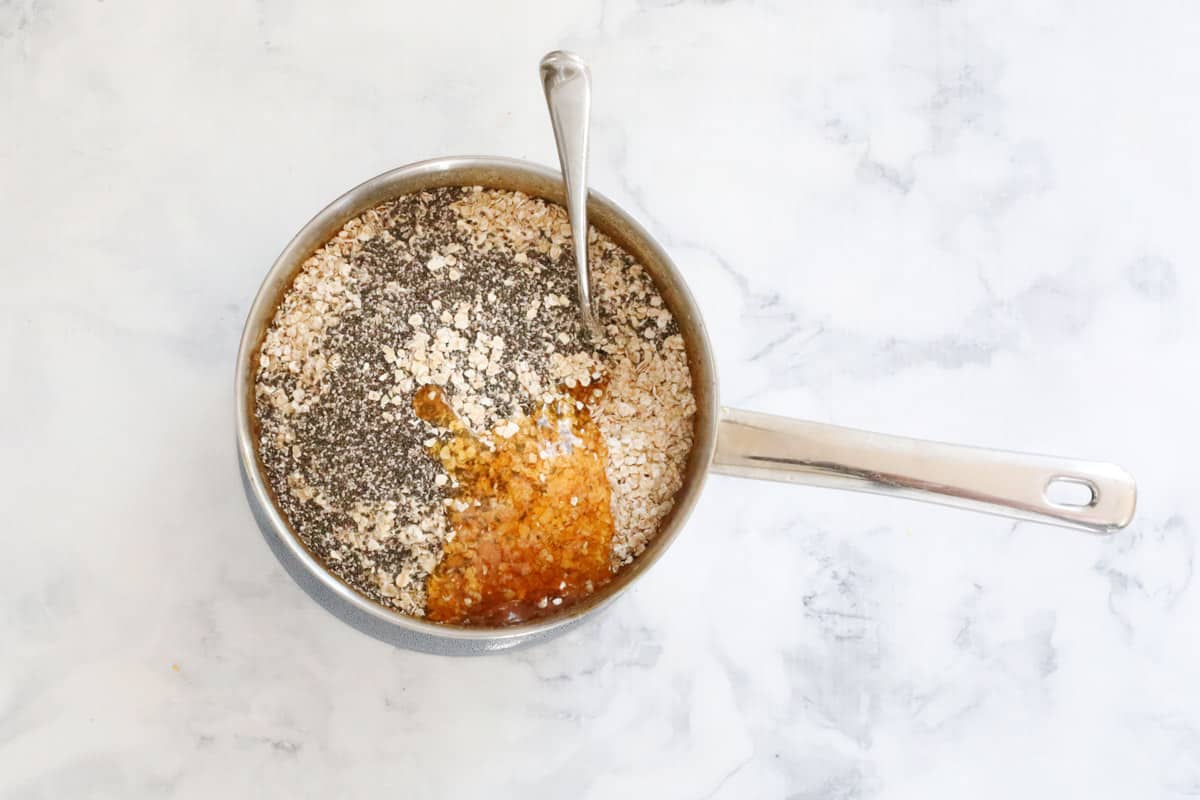 Rolled oats, chia and honey added to a pot with a spoon in it.