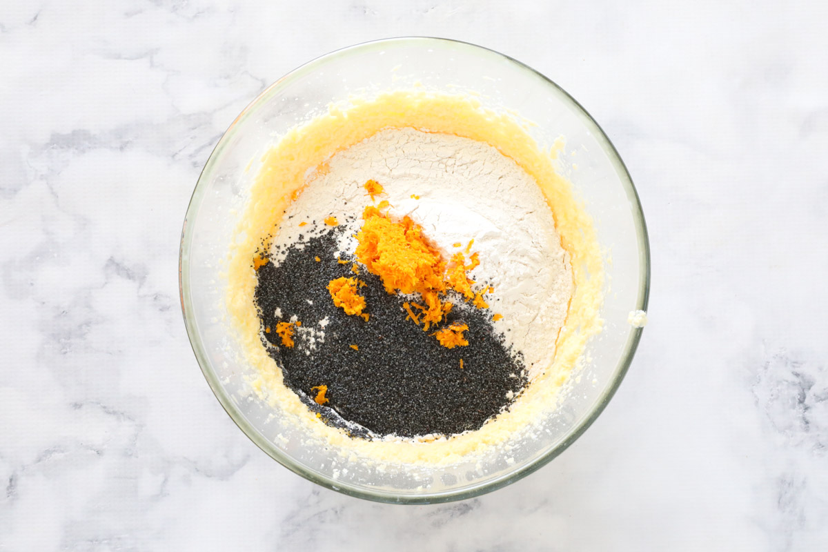A mixing bowl with orange zest, poppyseeds and flour on top of creamed wet ingredients