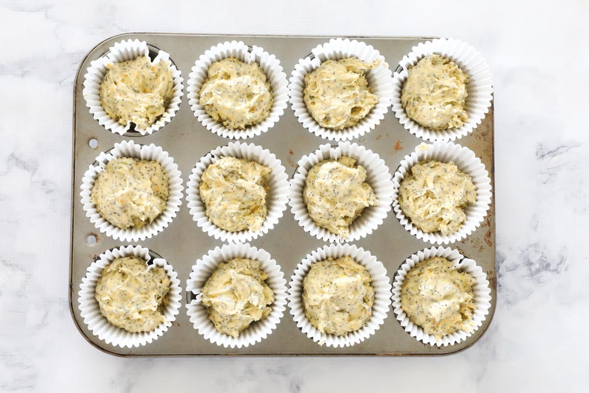 A 12 hole muffin tin lined with paper cases and filled with batter ready for baking