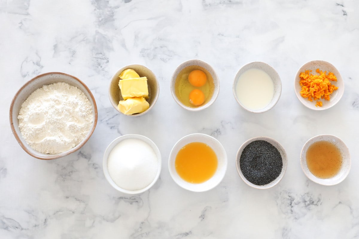 Ingredients for orange and poppyseed muffins in individual bowls on a marble counter