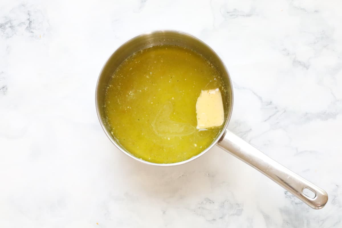 A saucepan on a marble surface with a rectangle of butter melting in vegetable stock
