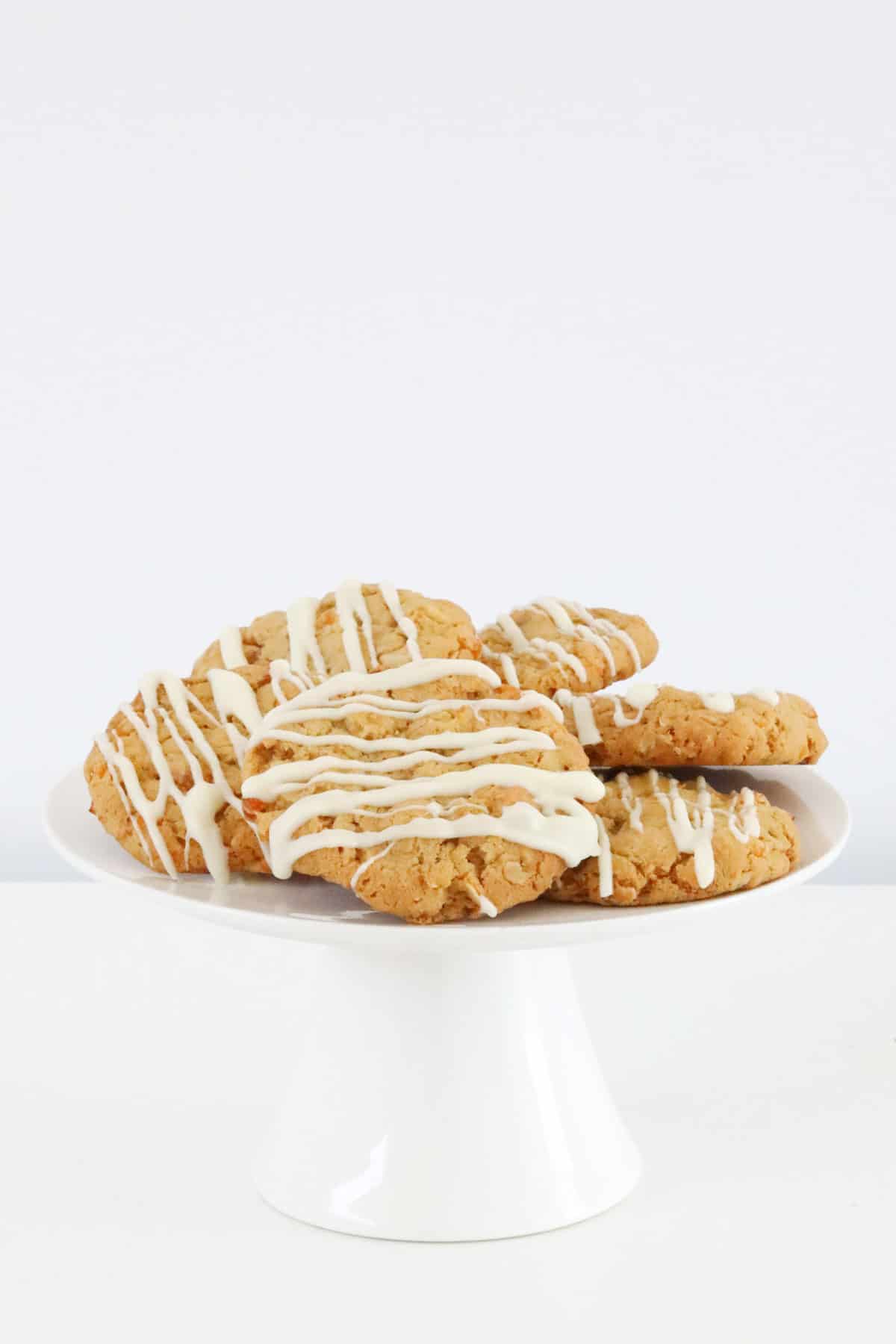 White chocolate drizzled over cookies on a white cake stand.
