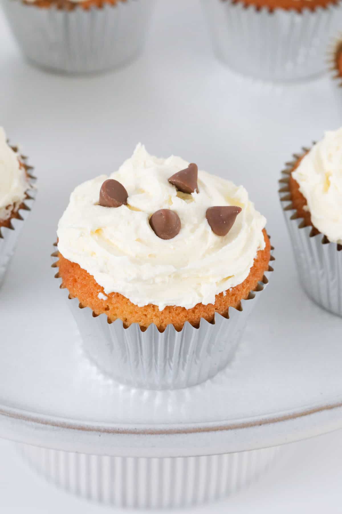 A cupcake topped with frosting and chocolate chips on a cake stand
