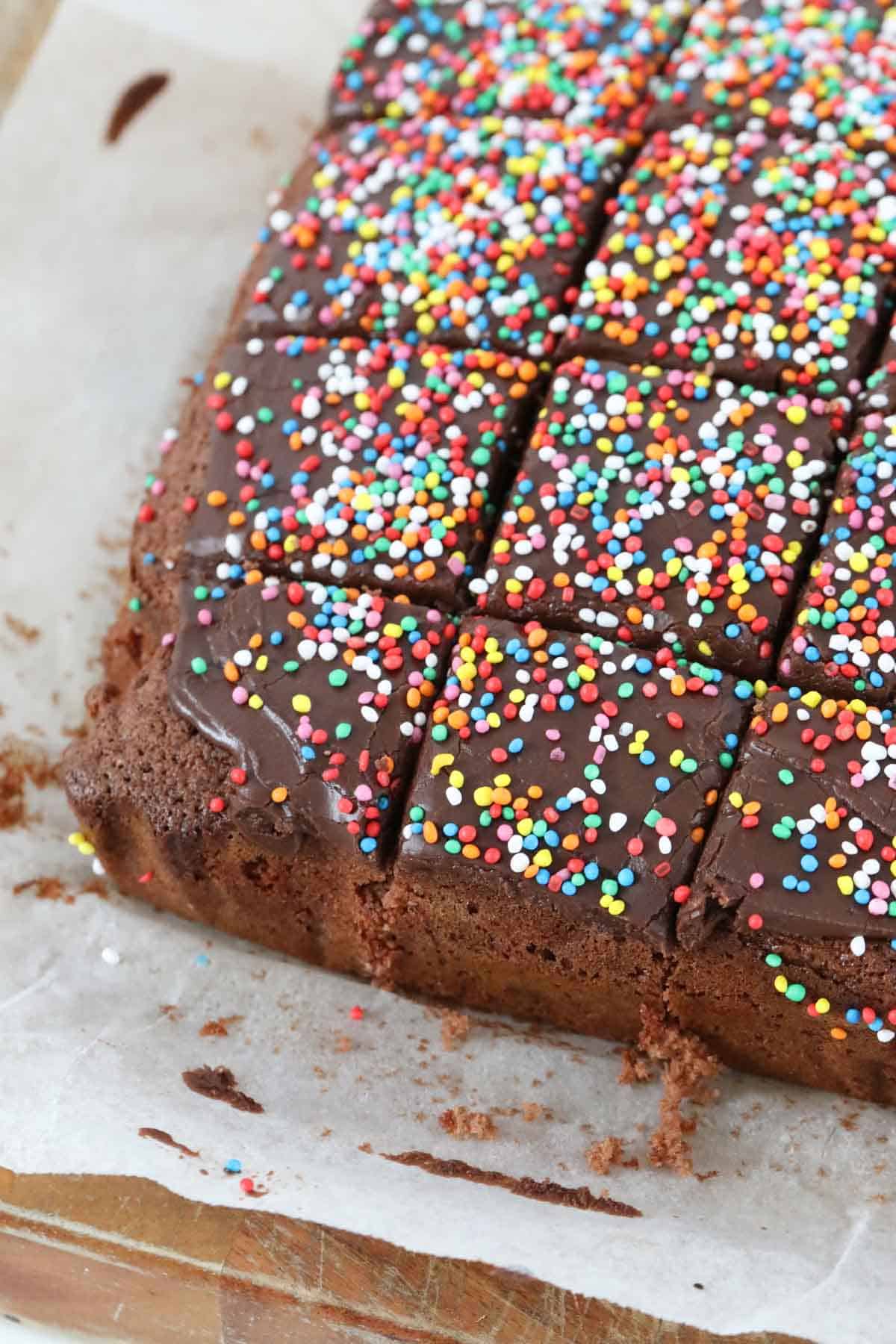 Cut chocolate cake with sprinkles on top, served on a wooden board.