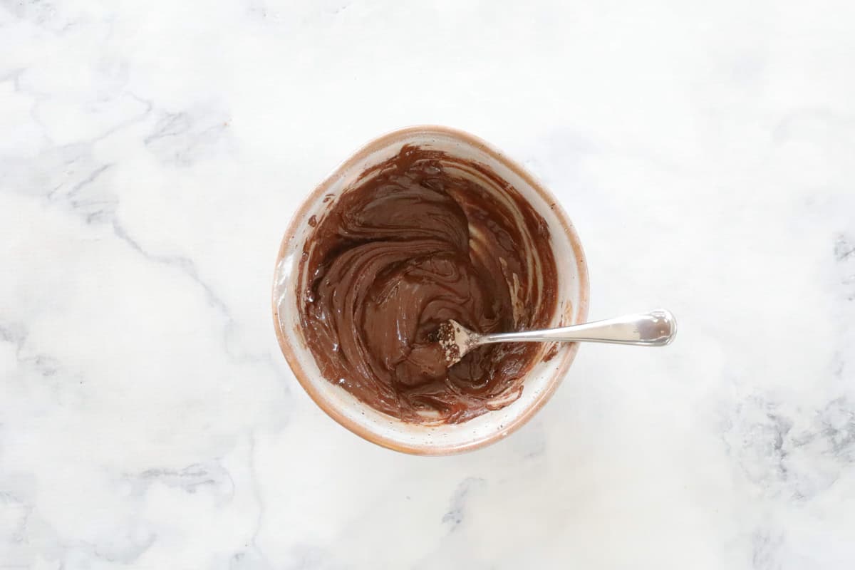 Chocolate icing in a bowl with a spoon.
