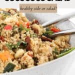 A bowl of veggie and couscous salad with a pair of silver salad servers.