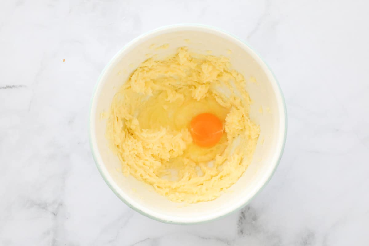 Egg in a mixing bowl with creamed butter and sugar.