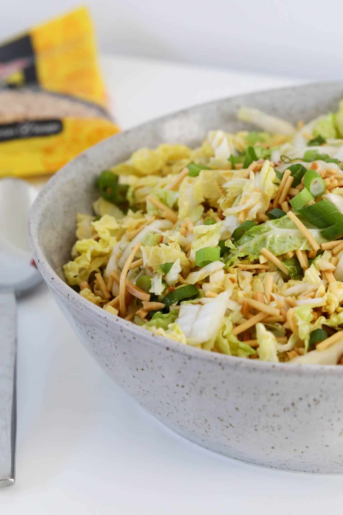 A bowl of salad with a packet of Chang's fried noodles placed on a table.